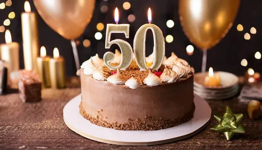 Chocolate birthday cake with "50" candles, surrounded by golden balloons and festive decorations, celebrating a milestone birthday.