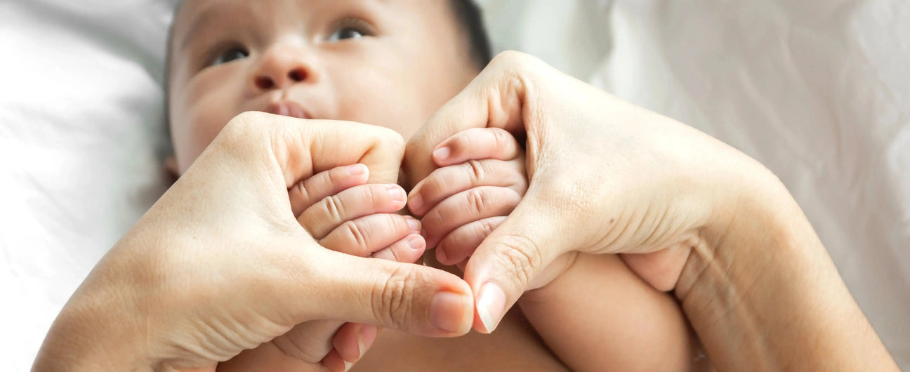 Two adult hands gently hold a newborn's feet, emphasizing warmth and tenderness; soft lighting creates a serene atmosphere.