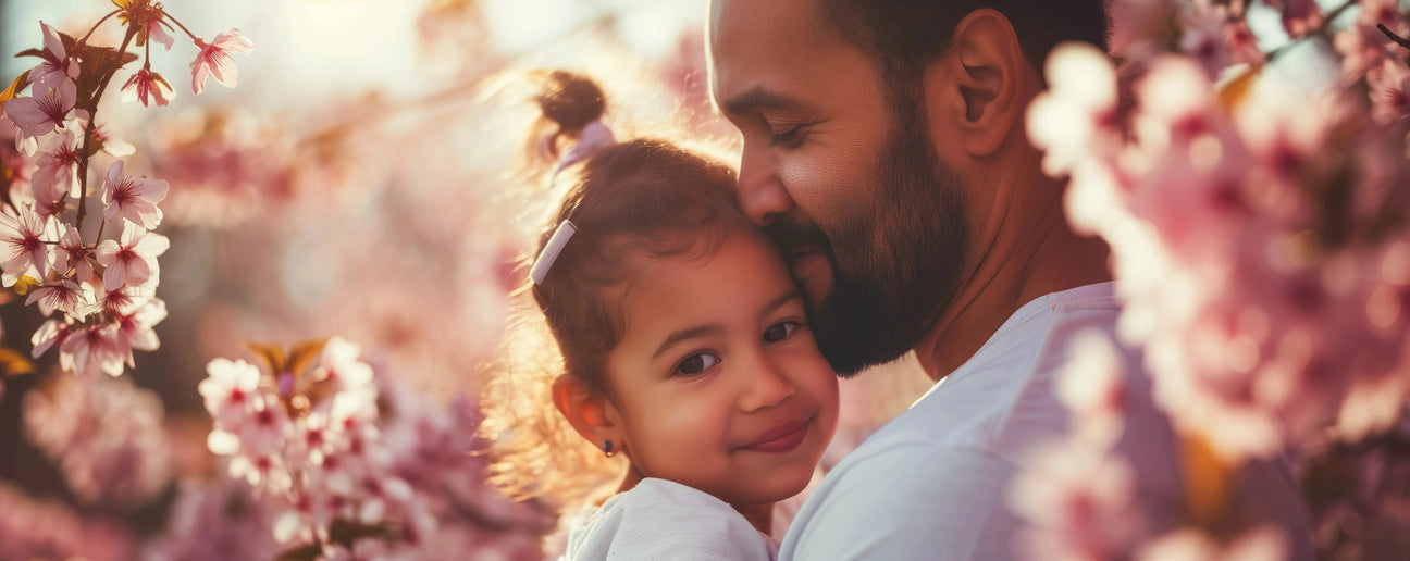A father hugs his daughter among blooming pink cherry blossoms, both smiling, capturing a warm, affectionate moment.